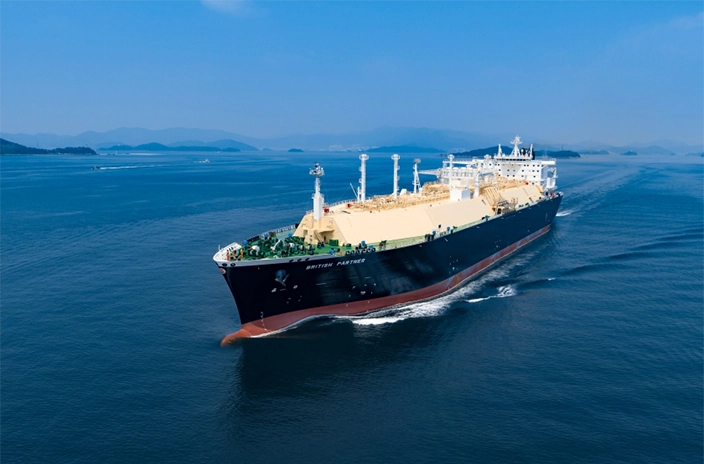 The LNG carrier from BP Shipping sails through calm blue waters under a clear sky, with distant mountains on the horizon.