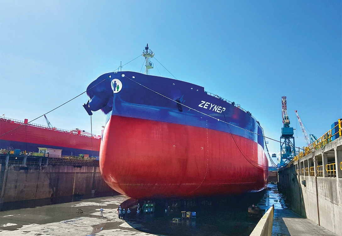 The vessel "Zeynep" is shown in a dry dock, featuring a blue and red hull with workers visible beneath it.