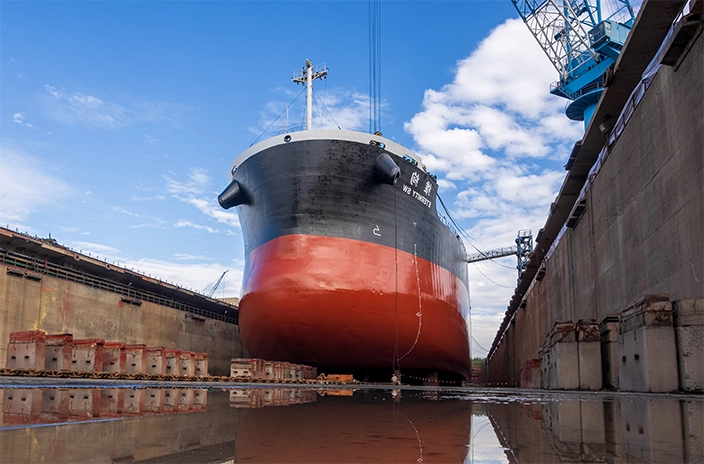 The bulk carrier "Eternity SW" from Shih Wei Navigation company in a dry dock, with its black and red hull resting on supports under a clear blue sky.