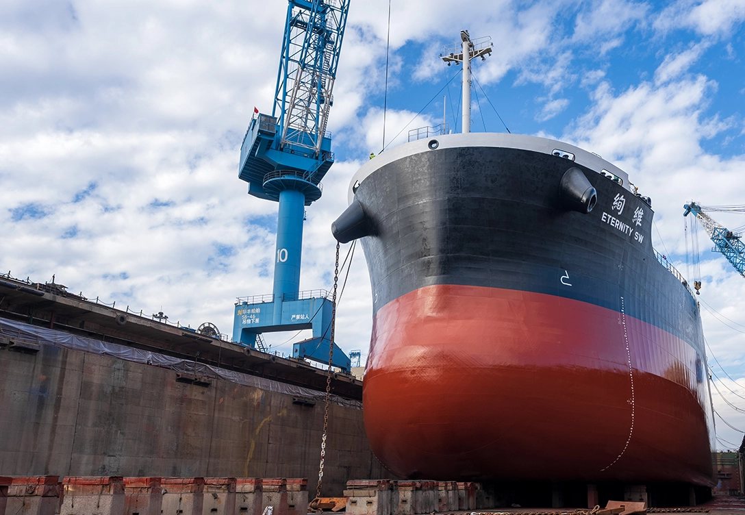 The bulk carrier "Eternity SW" from Shih Wei Navigation company in a dry dock, with its black and red hull resting on supports under a clear blue sky.