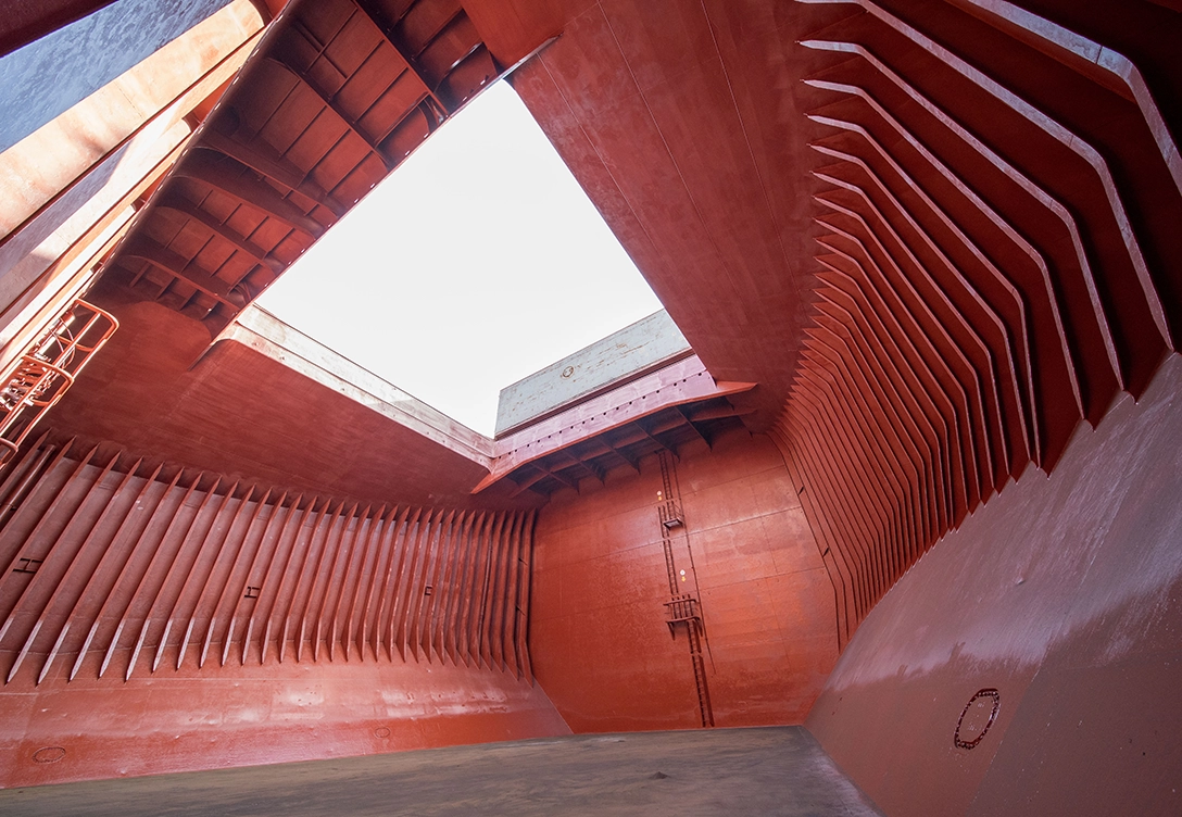 The interior of an empty bulk carrier cargo hold with red-painted walls.
