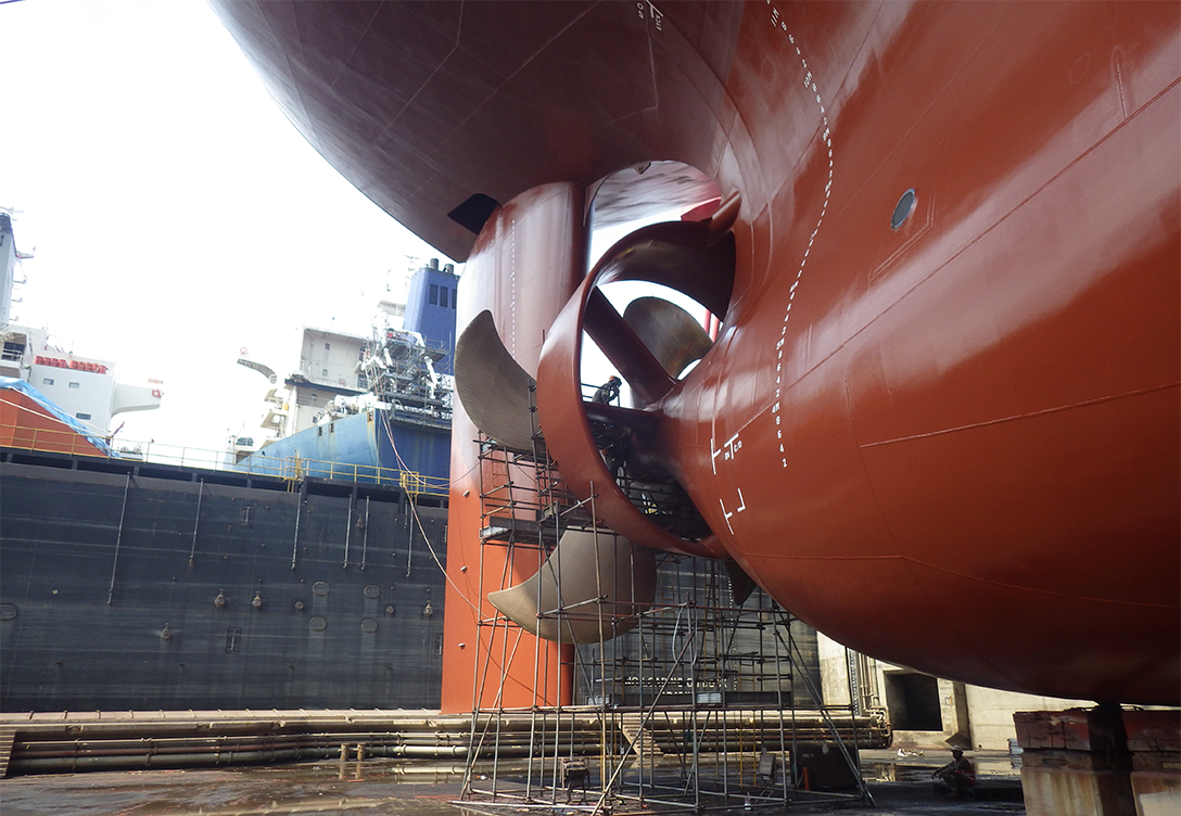 The image shows the hull of a Euronav vessel in dry dock, with its large rudder and propeller exposed, surrounded by scaffolding for maintenance, and other ships visible in the background.