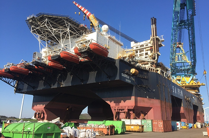 The Saipem 7000 semi-submersible crane vessel in a shipyard with its large cranes and lifeboats visible.