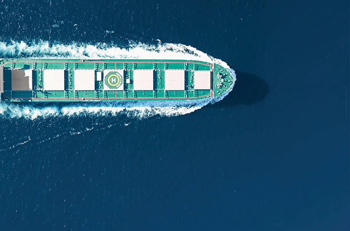 A top-down view of a U-Ming Marine Transport Corporation company's bulk carrier sailing through the deep blue ocean, with a green deck featuring large cargo holds and a helipad.