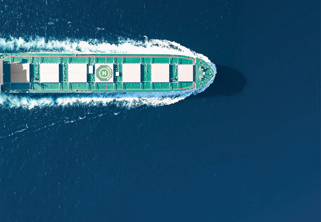 A top-down view of a U-Ming Marine Transport Corporation company's bulk carrier sailing through the deep blue ocean, with a green deck featuring large cargo holds and a helipad.