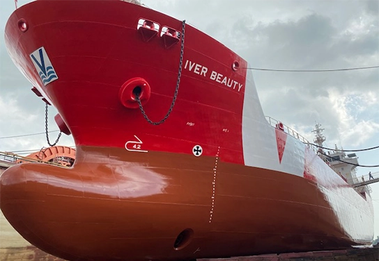 The vessel "Iver Beauty" from Vroon operator is shown in a shipyard, featuring a red and brown hull, coated with Hempaguard MaX.