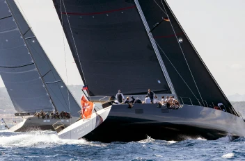 The superyacht Missy sailing at high speed on the water with its black sails fully raised, while another yacht sails nearby in the background.