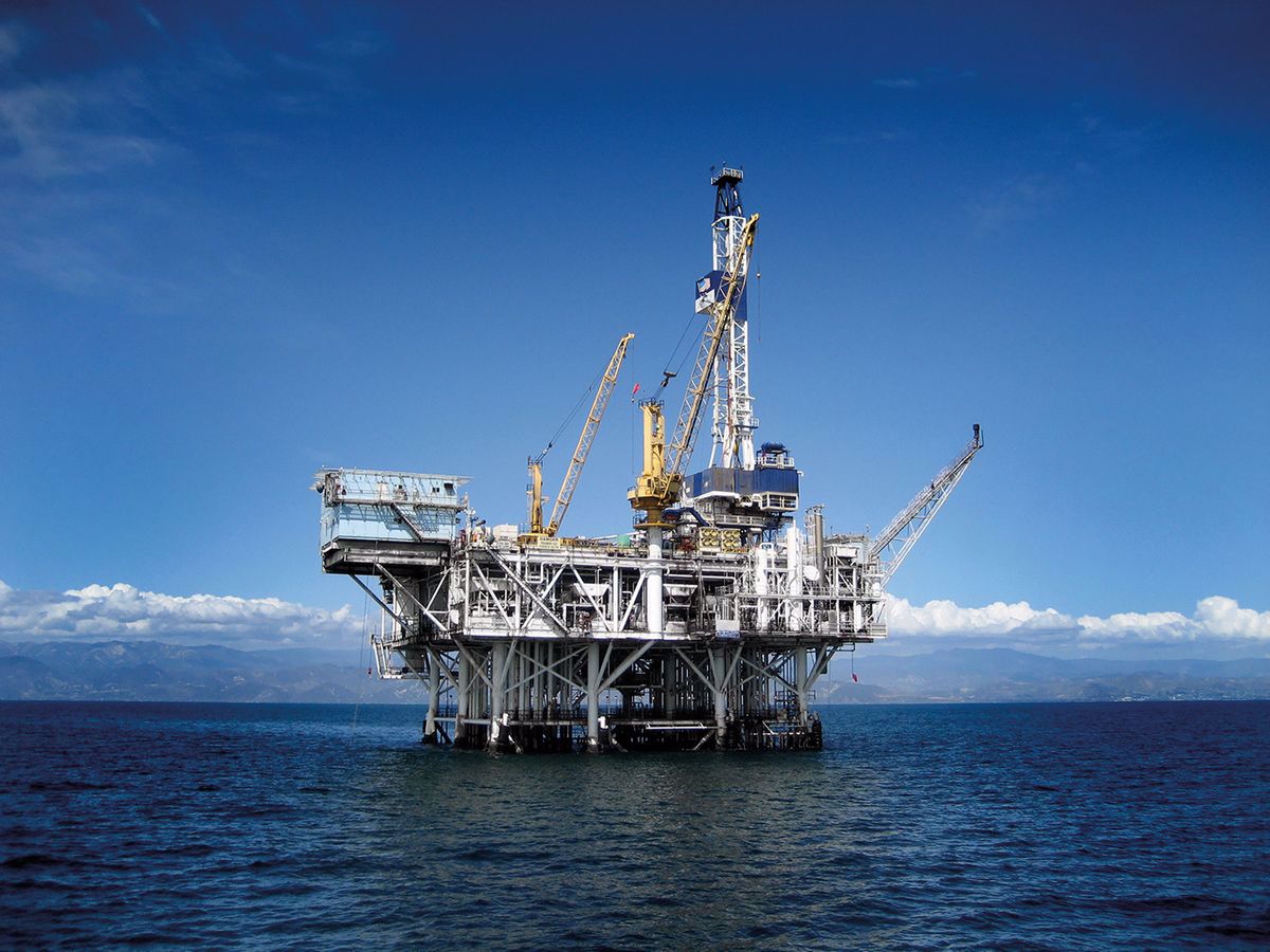 An offshore oil platform with cranes and equipment situated in the ocean under a clear blue sky.