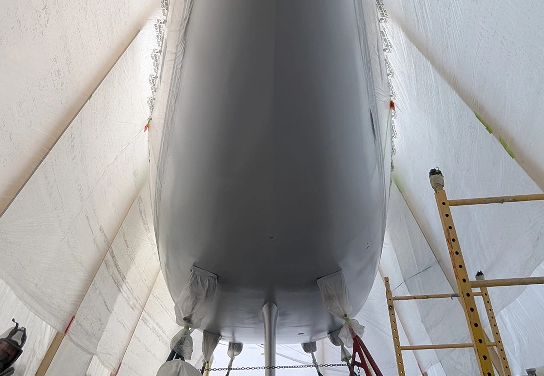 A large white boat is being painted inside a garage, with tools and paint supplies visible around it.