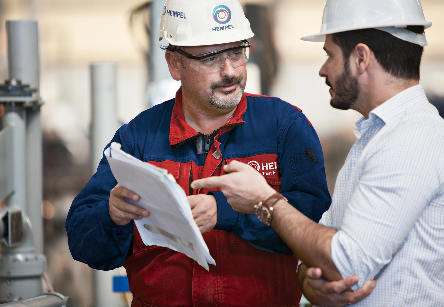 A coating advisor from Hempel is discussing a document with another man in a white shirt.