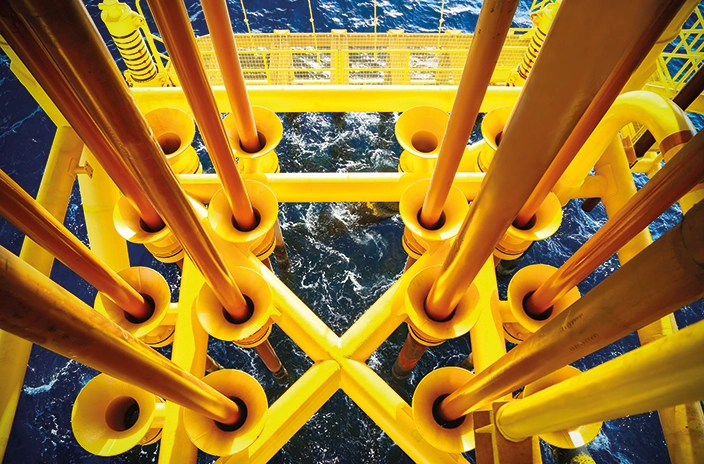 Yellow fuel drilling pipes arranged over ocean waves, part of an offshore oil rig structure.