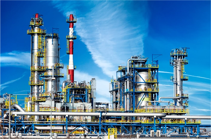 Industrial plant with large metal structures, pipes, and a red and white chimney against a bright blue sky.