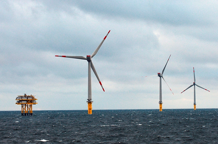 Wikinger offshore windfarm with three large wind turbines and an offshore platform in the distance on a cloudy day.
