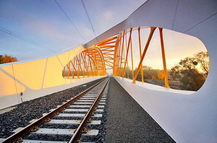 Railroad tracks leading through a Breclav bridge at sunset.