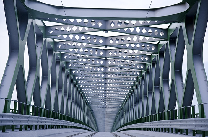 View of a steel railway bridge in Romania, with geometric patterns along its structure, extending into the distance.