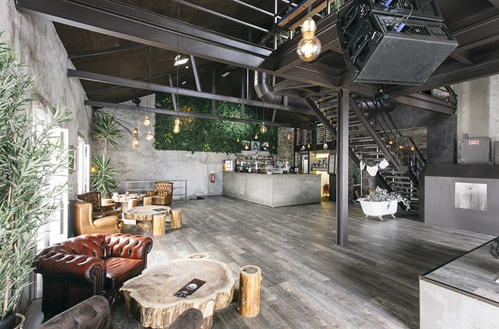 Rustic interior of Raiz cocktail bar with leather chairs, wooden tables, an industrial-style bar, plant wall, and exposed beams.