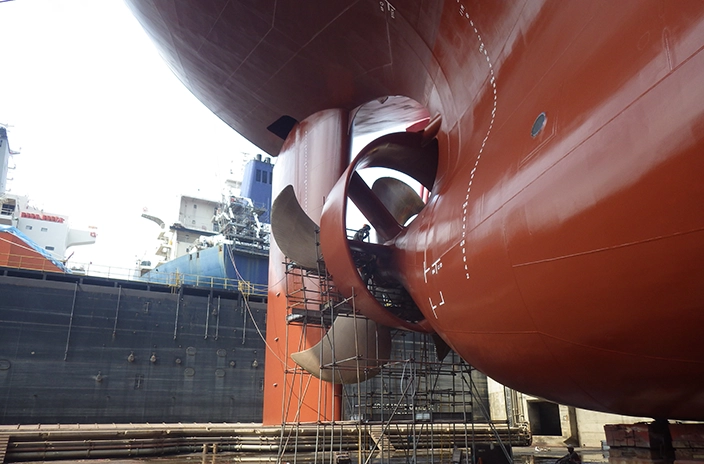 The image shows the hull of a Euronav vessel in dry dock, with its large rudder and propeller exposed, surrounded by scaffolding for maintenance, and other ships visible in the background.