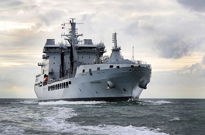 The UK Royal Navy's newbuild vessel sailing through rough seas, with its gray hull cutting through the water under an overcast sky.